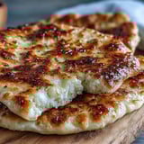 Soft, fluffy The Best Easy Garlic Naan Bread topped with fresh herbs, served warm beside a rich bowl of curry.