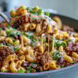 Hearty One-Pan High Protein Chili Mac topped with green onions and sour cream in a rustic bowl.