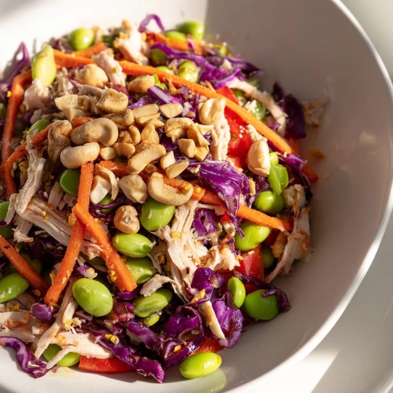 A vibrant serving suggestion for Edamame Crunch Chicken Salad with cashews, fresh lime wedges, and chopsticks on a wooden table.